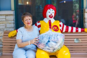 Trustee Higginson sits on a bench next to a Ronald McDonald statue and holds pop tabs with him.