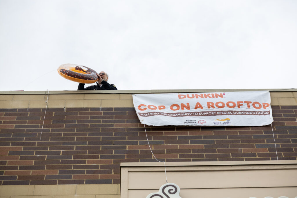 A police officer pretends to bite an inflatable donut on top of a Dunkin' Donuts roof.