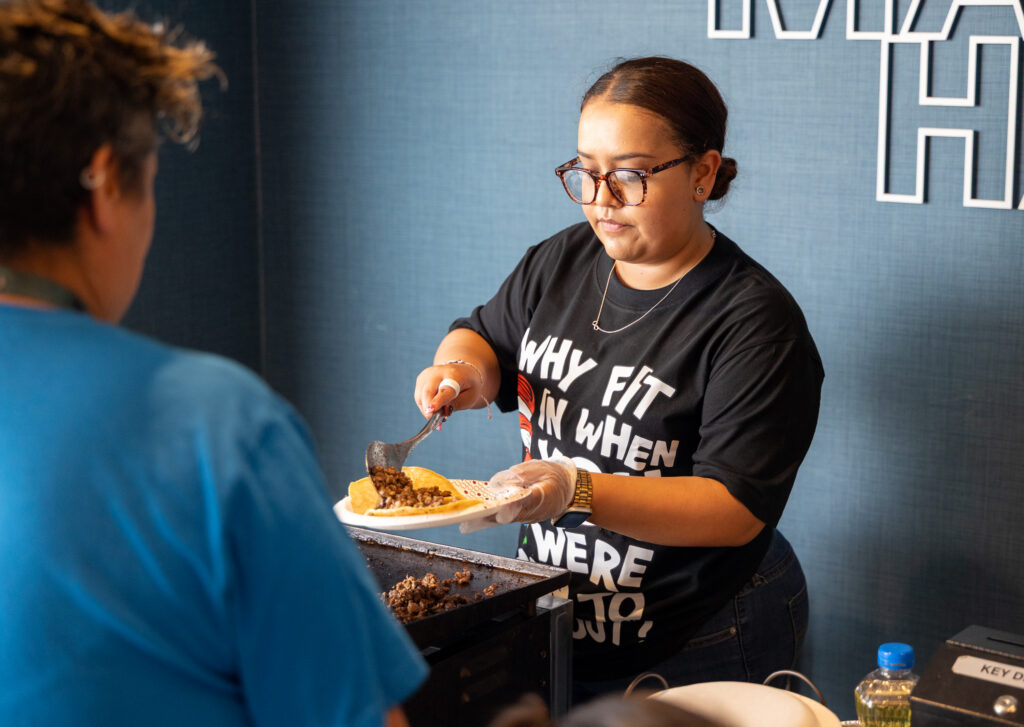 A woman ladles ingredients onto soft taco shells.