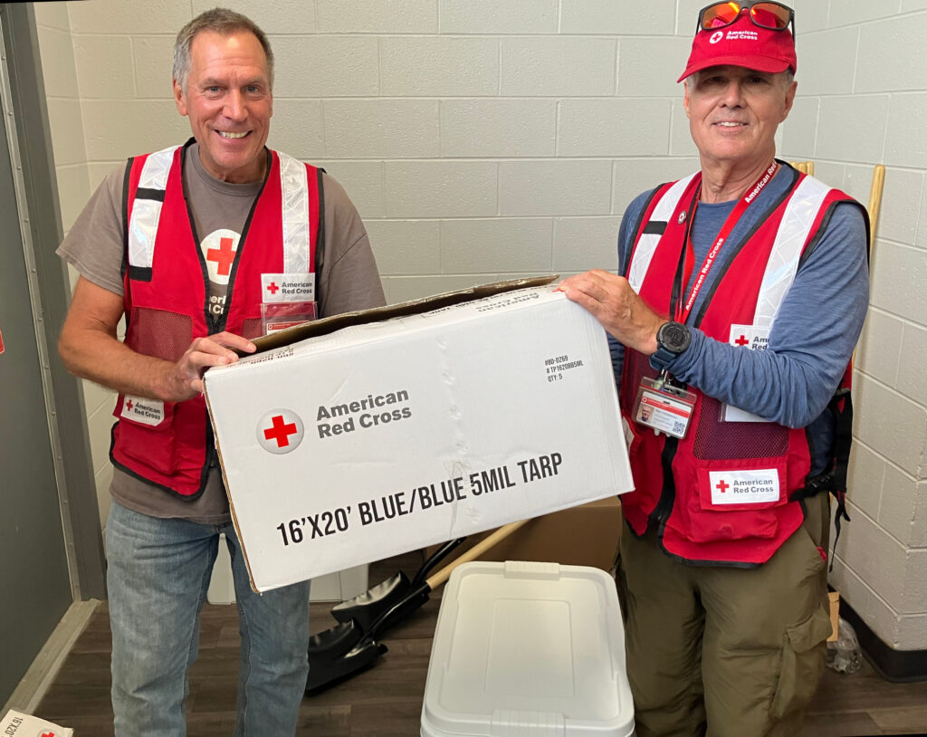 Two men hold a box of supplies form the American Red Cross.